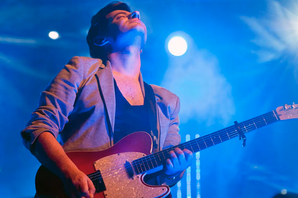 Lead guitarist under blue spotlight, Airport Impressions live at Beland Festival, Malta